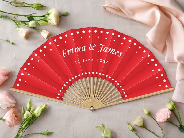 Personalised wedding fan "Polka Dots" with the names Emma & James, rows of polka dots along the edge and around the centre, red fabric with white print, on a wedding table
