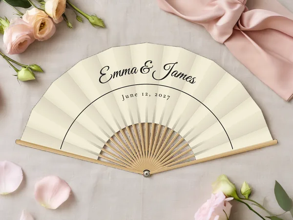Personalized wedding fan "Fine Line" with the names Emma & James, a single fine arched line below, ivory fabric with black print, on a wedding table