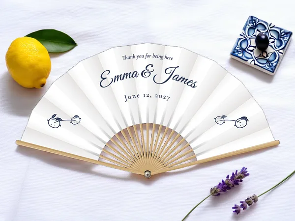Personalized wedding fan "Lemon Tree" with the names Emma & James, a small branch with two lemons on each side below, white fabric with navy blue print, on a wedding table