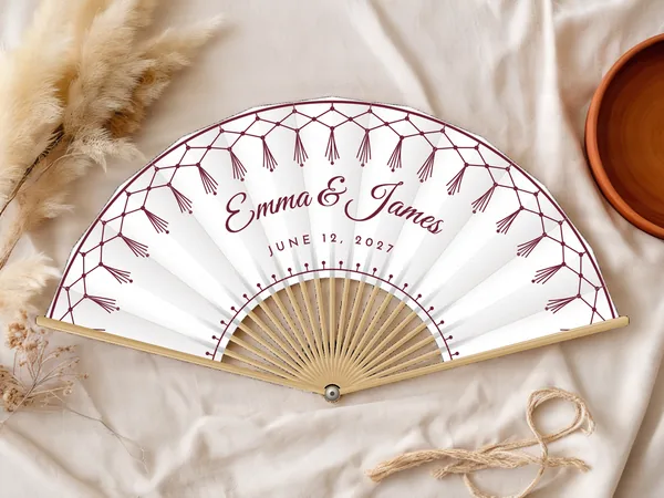 Personalized wedding fan "Macrame" with the names Emma & James, a tasseled macrame fringe along the edge, white fabric with burgundy print, on a wedding table