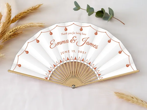 Personalized wedding fan "String Lights" with the names Emma & James, a string of light bulbs along the edge and bunting along the bottom, white fabric with terracotta print, on a wedding table
